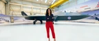 A smiling person standing in front of modern fighter jet in an aircraft hanger.
