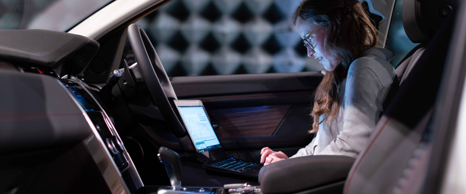 A person sitting in a car looking at its performance data on a laptop.