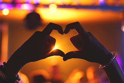 A person making the heart symbol with their hands in a brightly lit club.