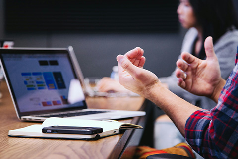 A persons hands gesturing in front of a laptop showing statistics.