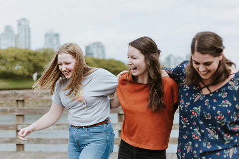 Three students walking and laughing, arm in arm.