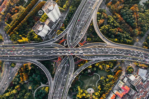 A view from above of a motorway with several on and off ramps. It is surrounded by trees in autumnal colours.
