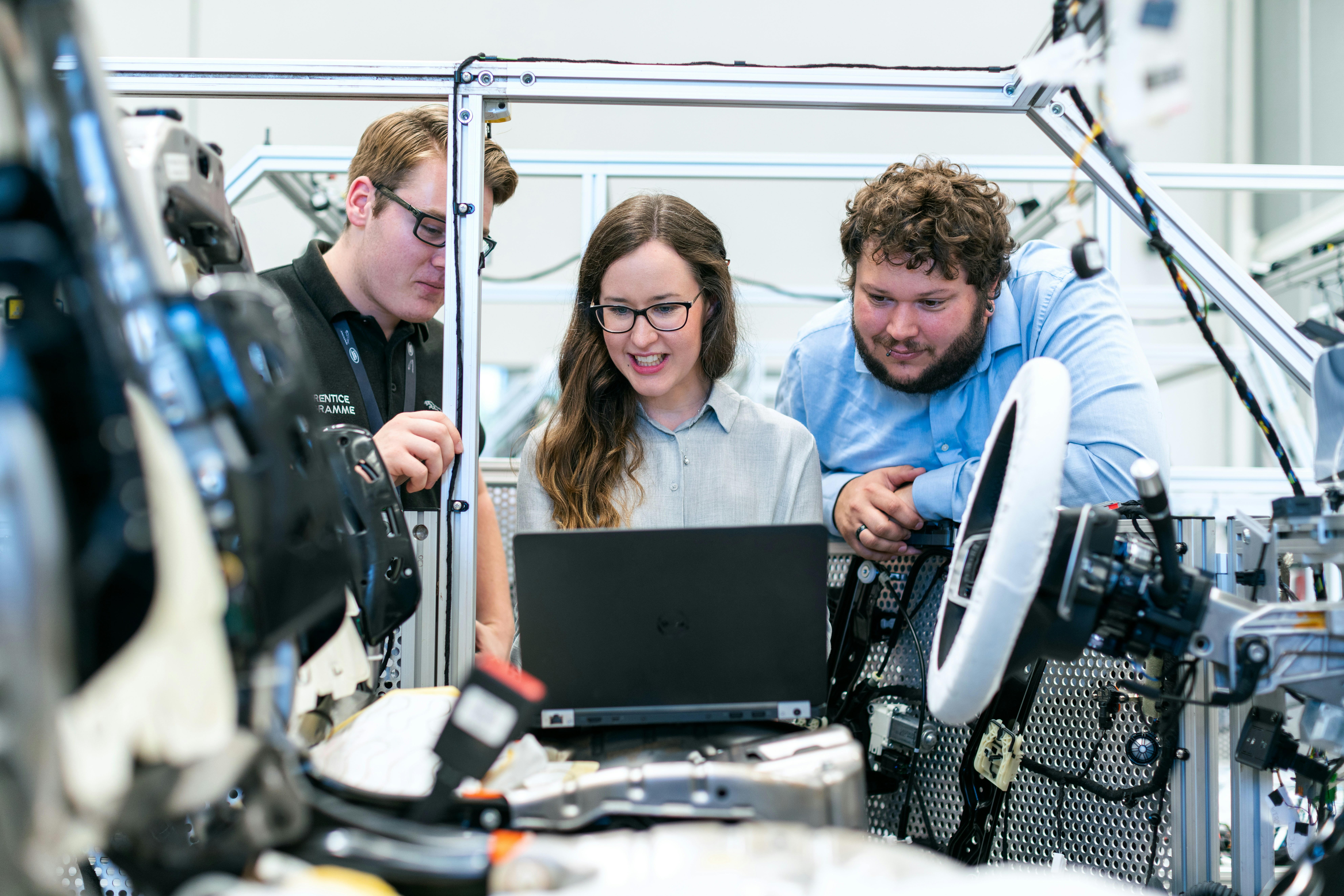 Students look at a laptop whilst working on a car.